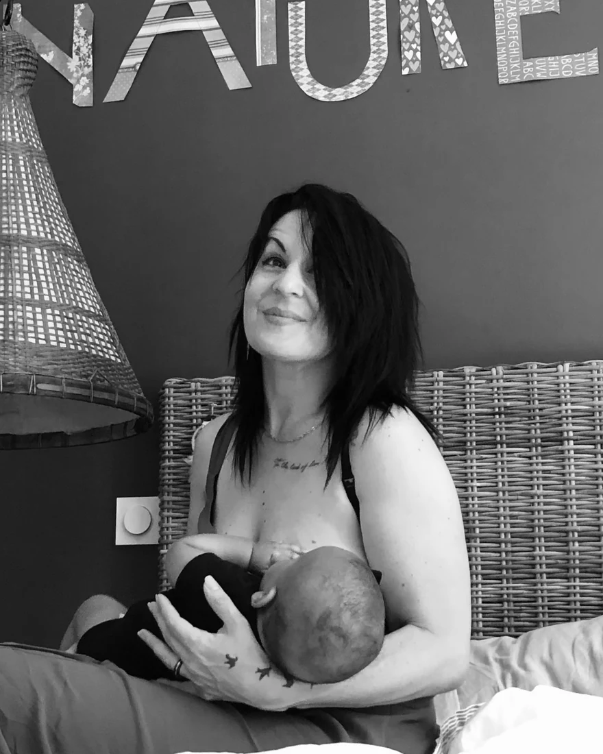 Aurélie allaitant son bébé, assise sur son lit.