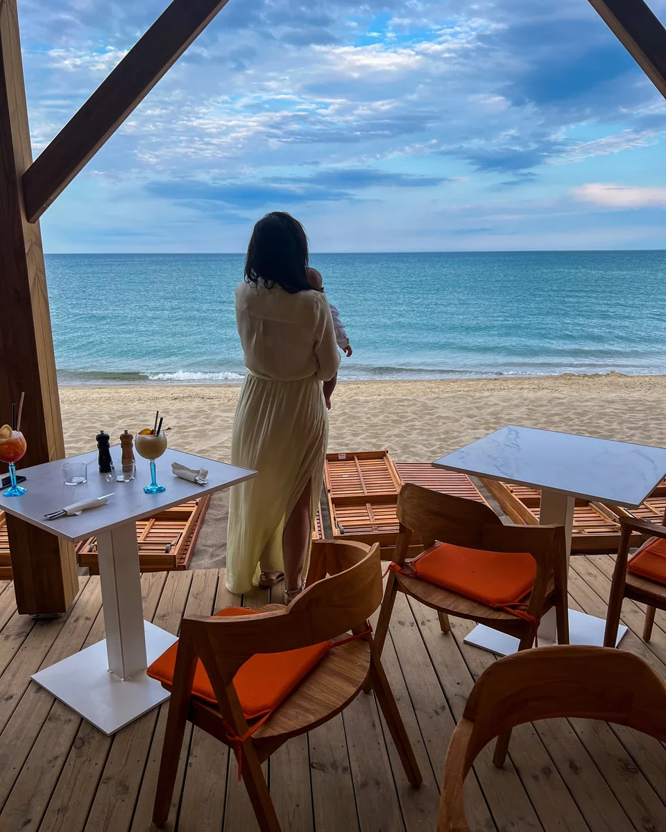 Aurélie de dos, son bébé dans les bras, face à la mer.